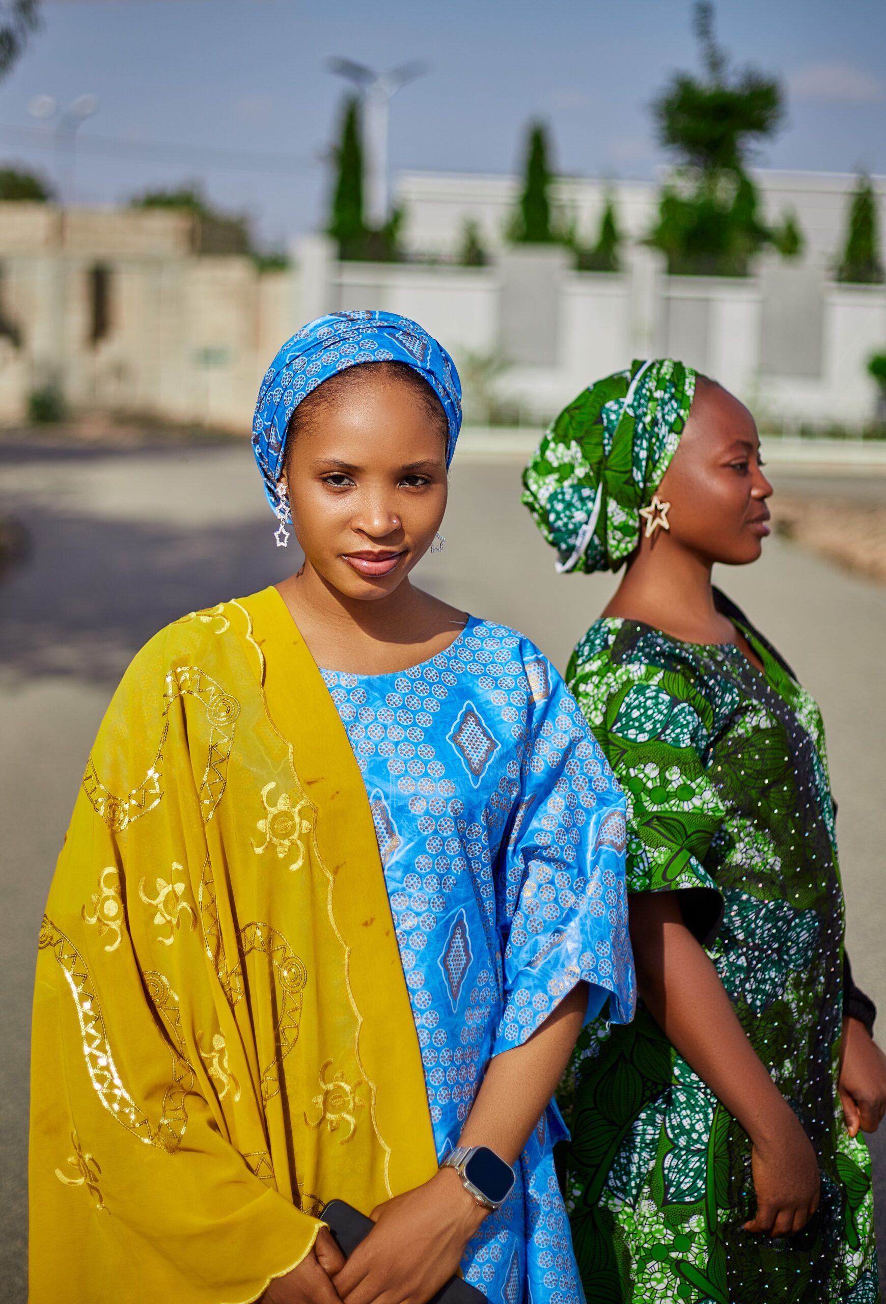 Two women in vibrant African attire posing outside, showcasing cultural elegance.